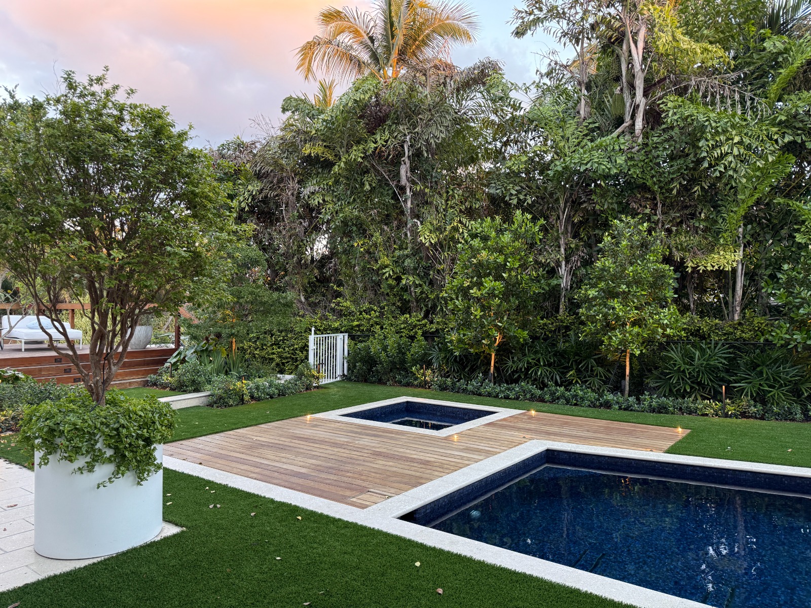 Jardín tropical al atardecer con jacuzzi y deck en madera